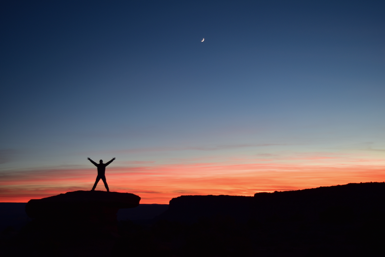 Person silhouetted agains a sunset, with the moon shining above them.